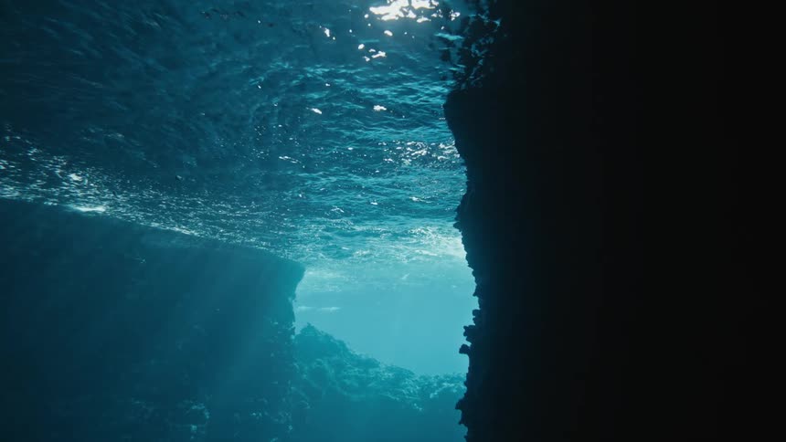 Sunlight filters through the surface of water illuminating a rocky underwater cavern