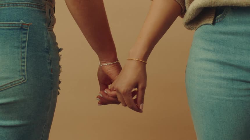 A close up of two women holding hands against a beige background