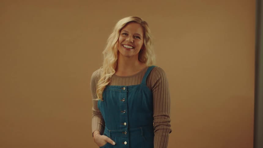 Woman wearing overalls is smiling and doing a pose