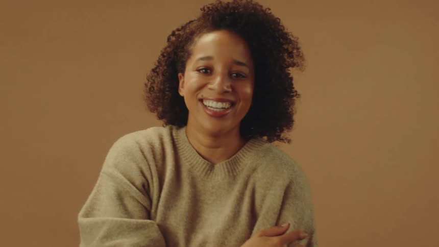 A woman is wearing a sweater while she smiles and laughs indoors