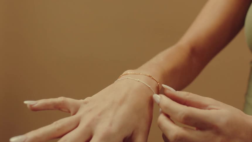 A womans wrist adorned with a delicate gold bracelet with their hand extended and fingers slightly curved against a soft muted background