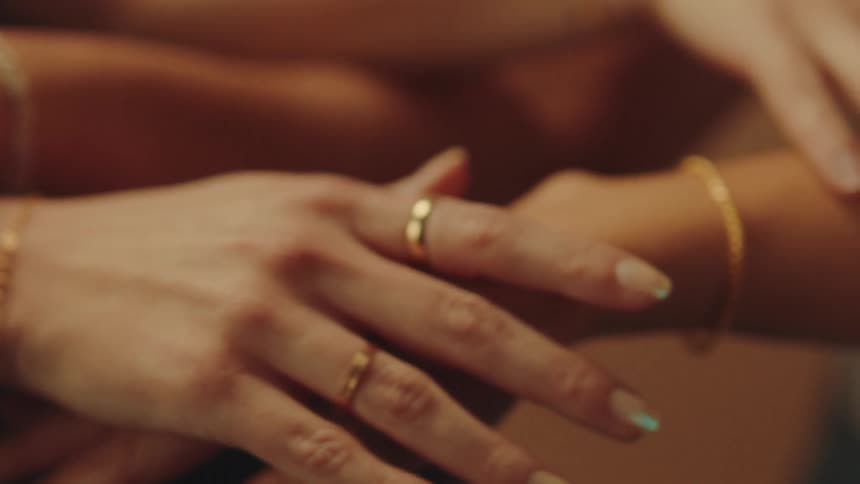Several arms adorned with delicate gold chain bracelets are intertwined against a softly lit background