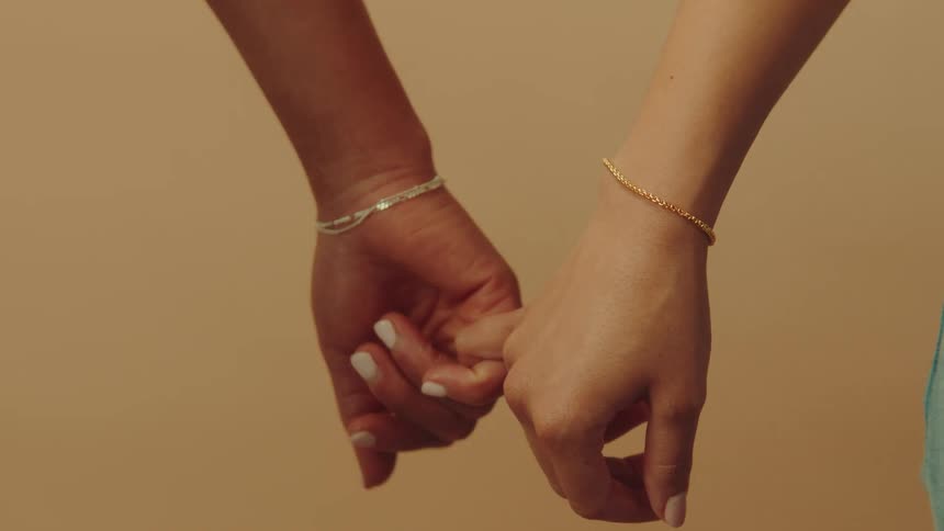 Two female friends are intertwining their hands together