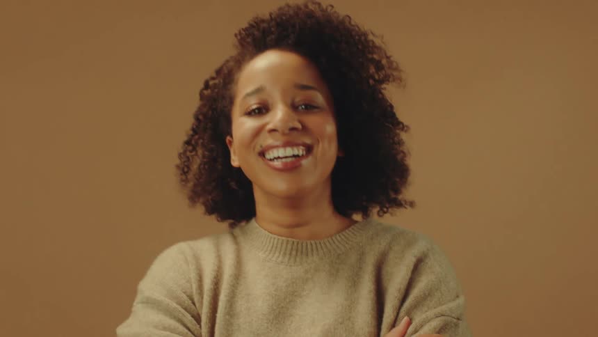 Woman is smiling and crossing her arms while standing in a room