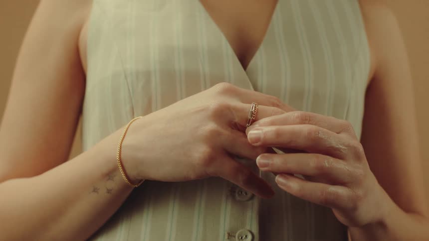 A person in a pinstriped vest adjusts a gold ring on their finger with a delicate bracelet visible on their wrist