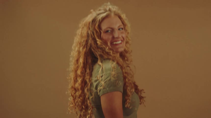 Long curly haired female modeling pair of jeans against brown backdrop