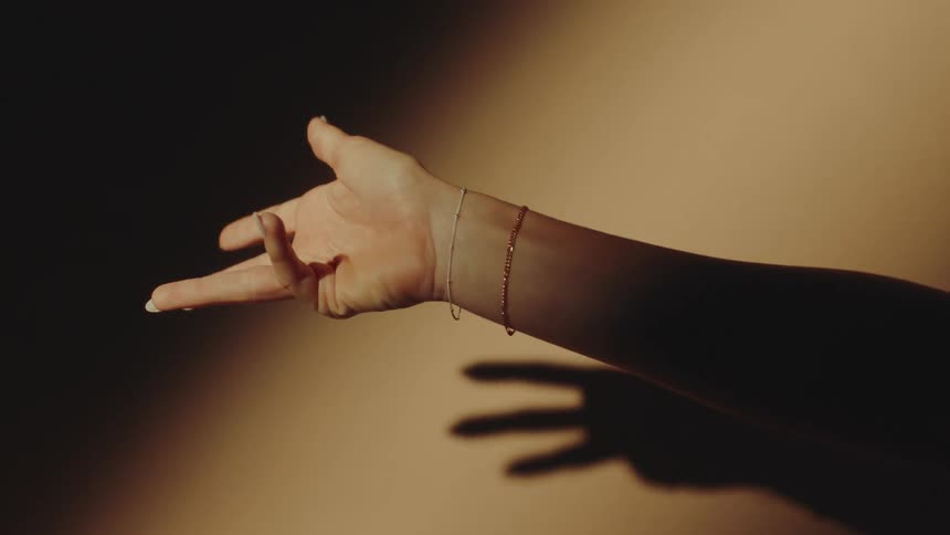 A female hand with a bracelet and she is moving her fingers making a shadow on the wall