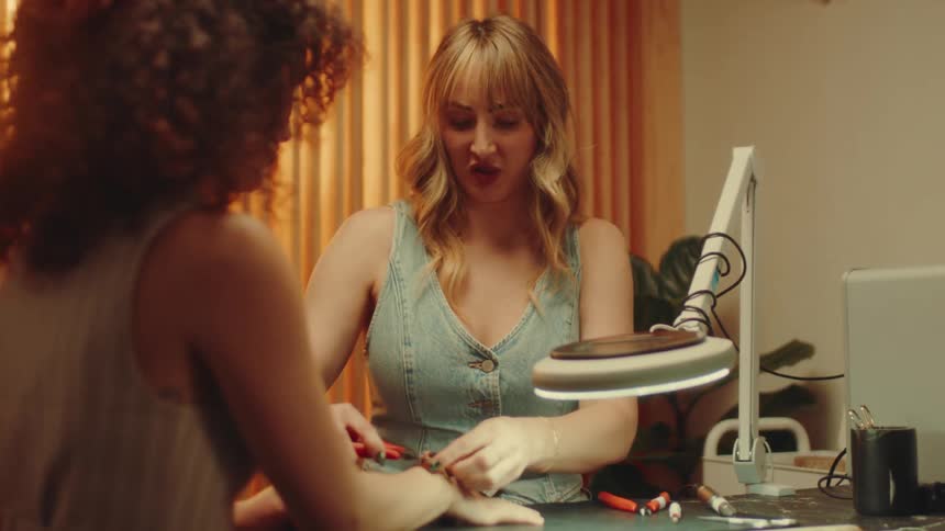Two women are sitting across from each other and the blonde one is moving the light to see the other womans hand better