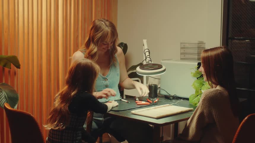 Woman placing an accessory on the wrist of a little girl who has her hand extended on a table