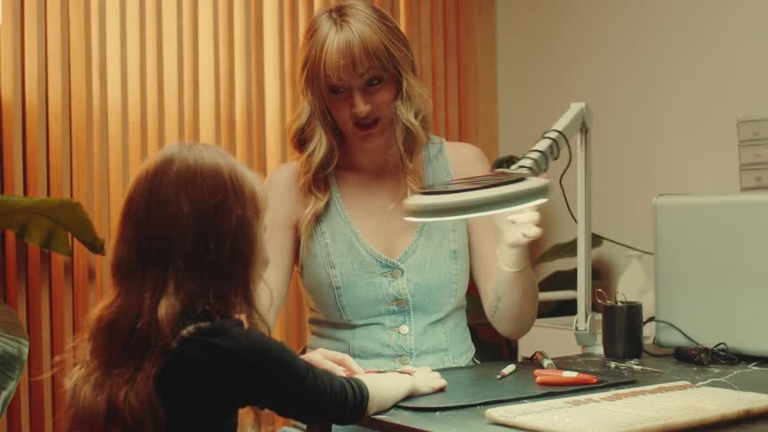 A woman adjusts a gold bracelet on a girls wrist in a welllit studio beneath a magnifying glass lamp