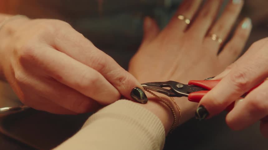 Pair of hands with pliers carefully placing a bracelet on a persons wrist