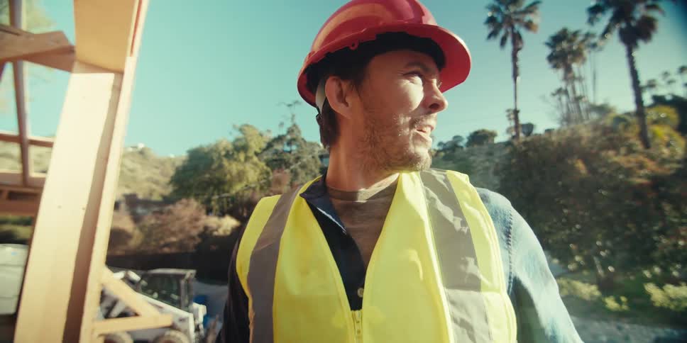 Man wearing a protective helmet and a green identification vest outside a construction site