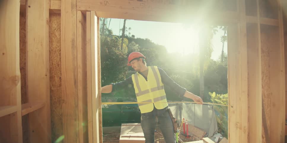 Man working on a construction site and using a tape measure to measure the opening of a door