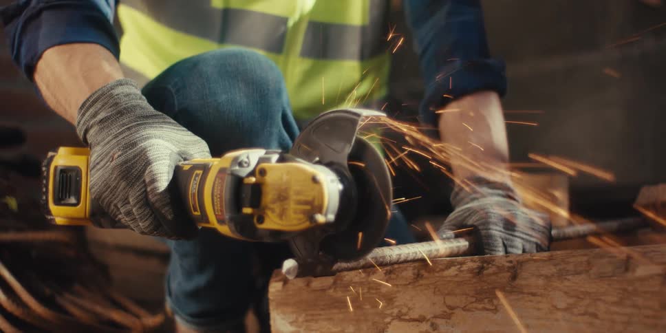 Worker using a power tool to cut a metal bar with sparks being generated during the process