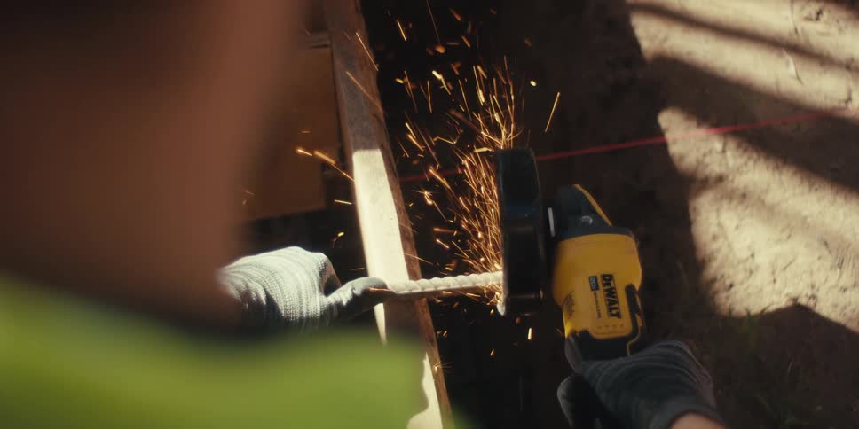Male construction worker creates sparks while cutting a metal bar with a power tool