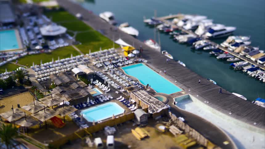 People walk along the path between multiple swimming pools and a dock