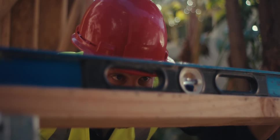 Carpenter working on a construction site uses a level to check a board