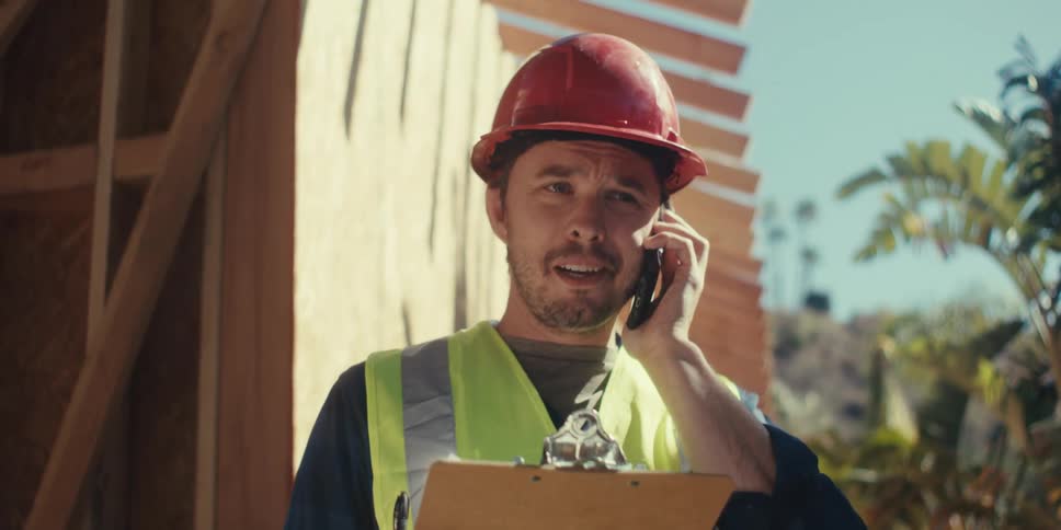 A construction worker is on site and talking on his cell phone