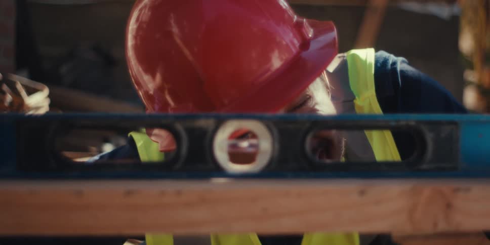 Man with helmet and identification vest working on a construction site and looking through a level tool