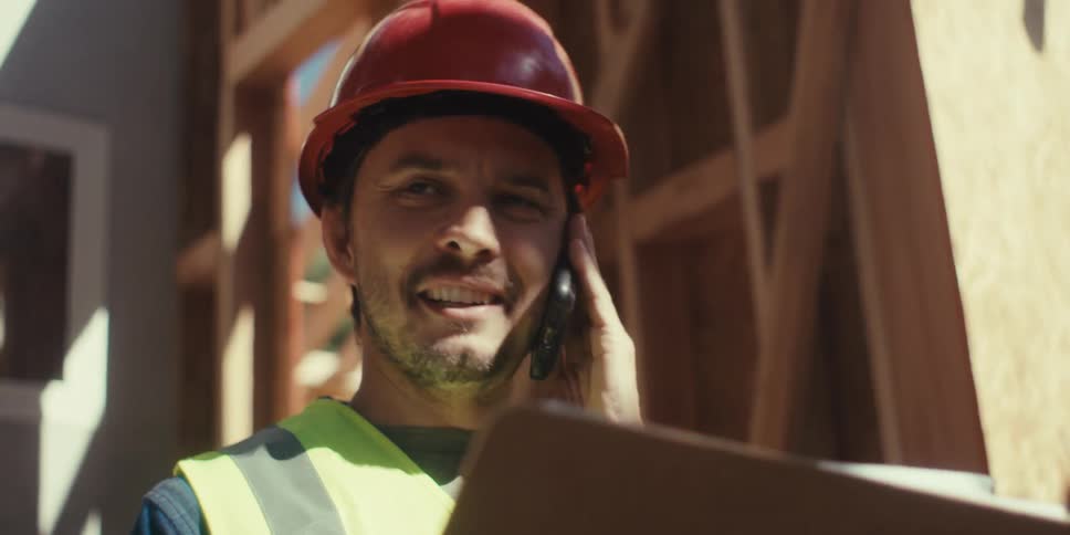 Man in helmet working on construction site and talking on phone