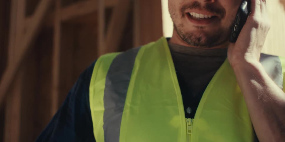 Construction worker is smiling at the job site while talking on a cellphone