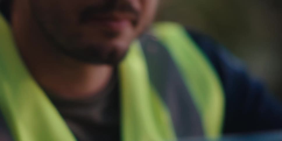 A construction worker wearing a visibility vest and red hard hat uses a level at a construction site