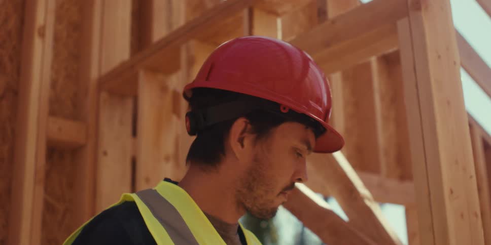 Male construction worker examines the wooden frame of an unfinished wooden structure on a sunny day