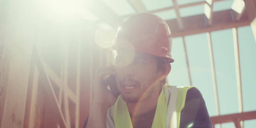 Man at a construction site wearing a protective helmet talking on a phone call