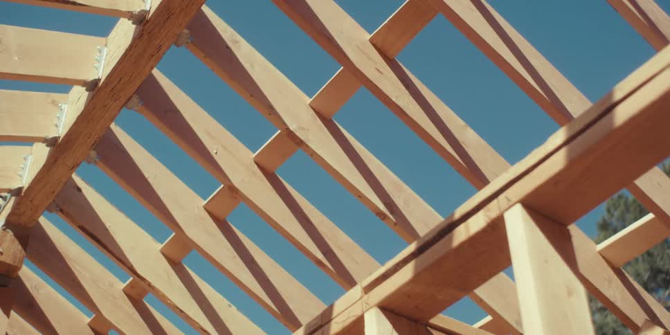The intricate patterns of a timber roof truss against a clear blue sky