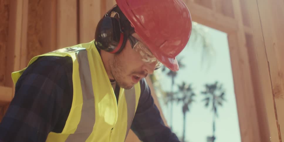 Man wearing safety glasses and a helmet using a wood cutting tool at a construction site