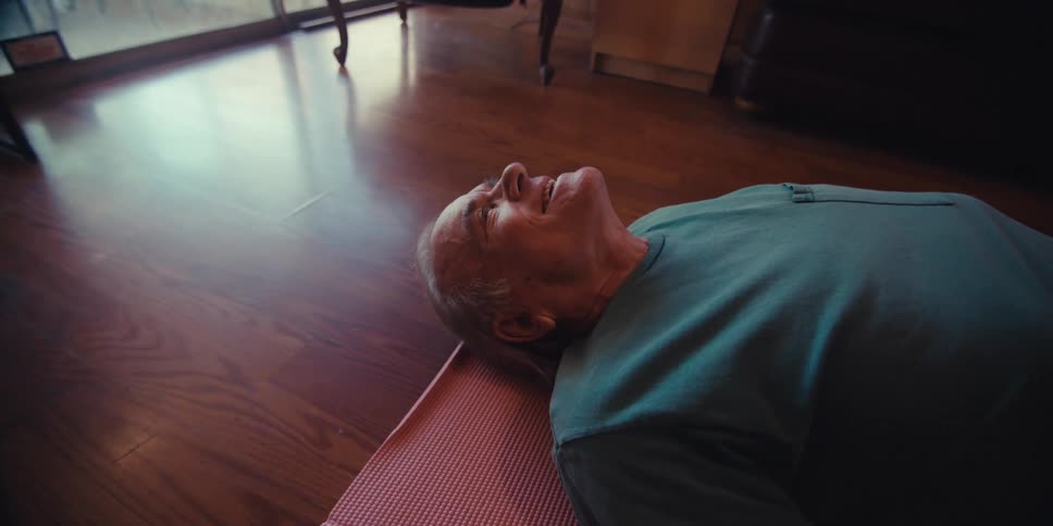 Elderly man is laying on a mat on the hardwood floor