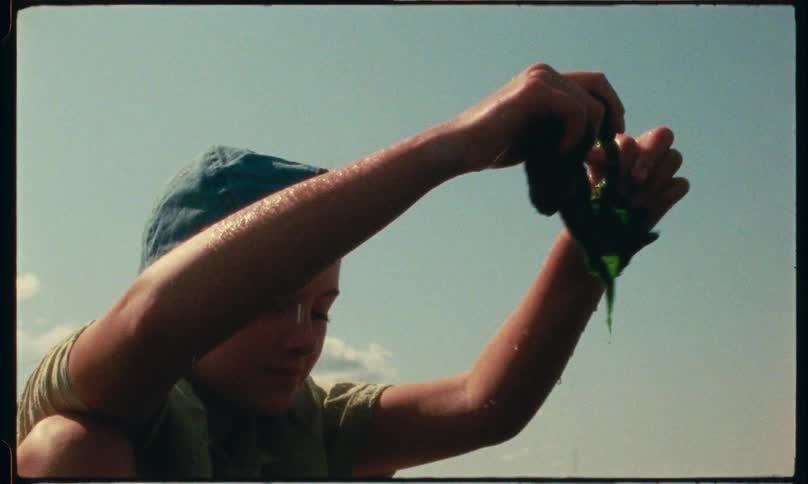 A girl crouches on coastal rocks playing with wet green seaweed