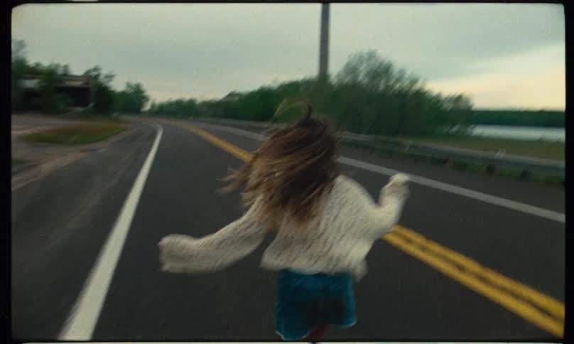 A girl is shown from behind running down the street in a rural area