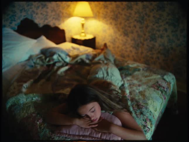 A woman rests on a bed illuminated by the cozy glow of a warm table lamp