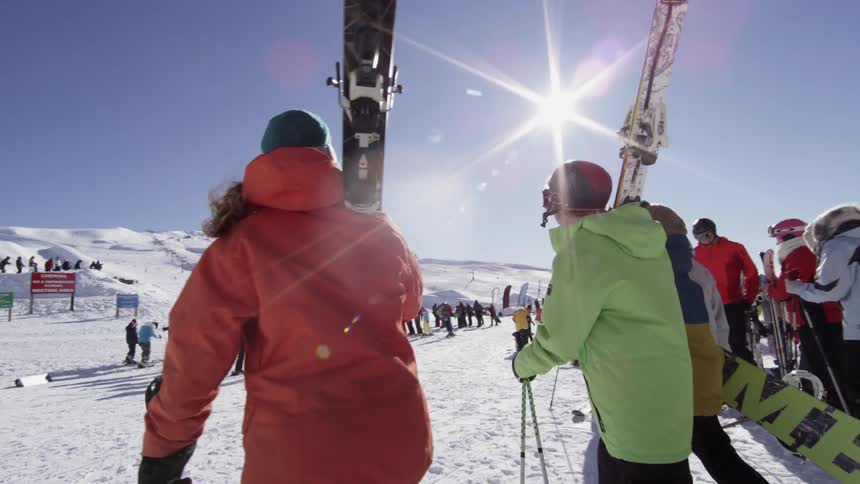 A group of people carry ski equipment over a snowy terrain