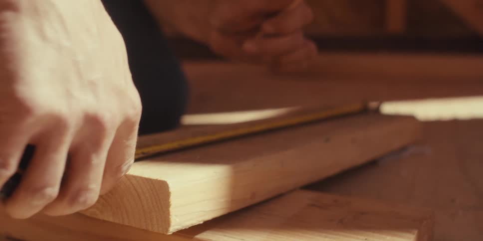 A construction worker marks a piece of wood