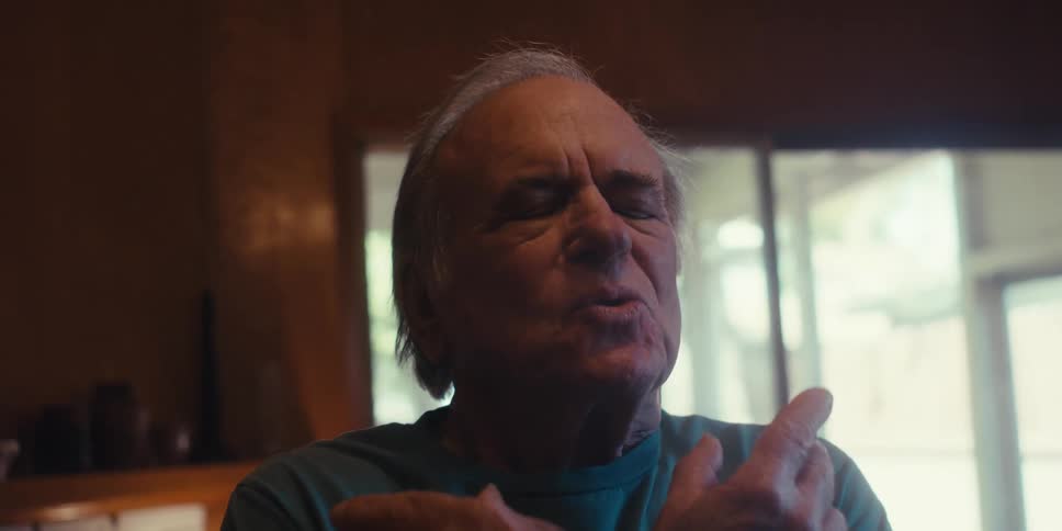 An elderly man stands on the living room practicing breathing exercises in a dimly lit room