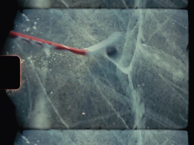 A boy wearing ice skates on a frozen pond is doing puck maneuverswith a hockey stick before skating away from the camera while continuing to control the puck
