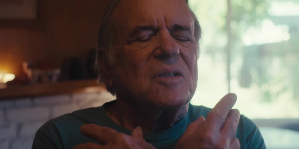 An elderly man stands on the living room floor practicing breathing exercises with sunlight streaming through the windows
