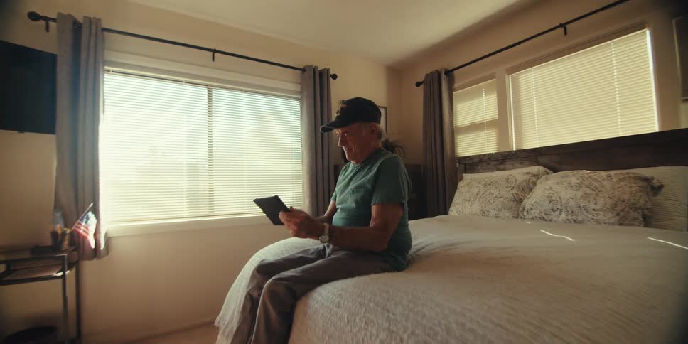 Elderly man sitting on bed laughing out loud