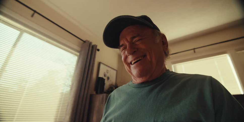Elderly man with happy facial expression while sitting on a bed interacting with a tablet