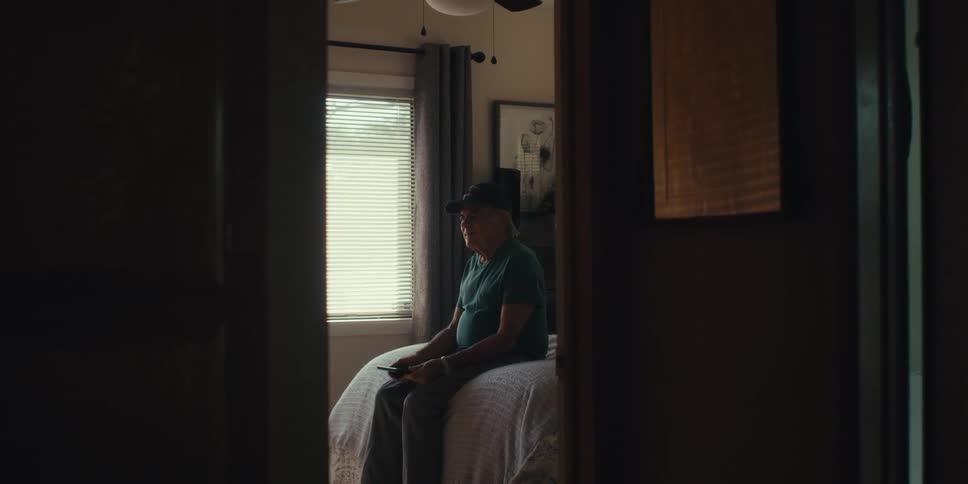 Man sitting on a bed looking at a tablet and being happy