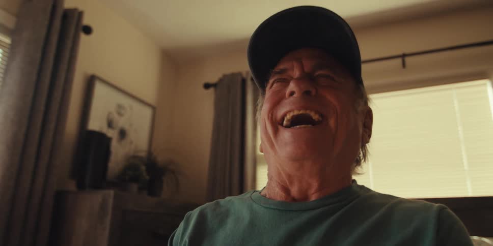 Elderly man sitting on bed laughing looking at a tablet