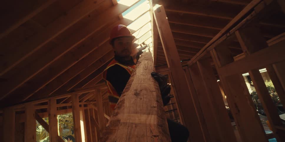 Two workers carefully remove a wooden beam from the framework of a house under construction