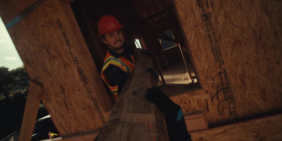 Construction workers wearing helmets and safety clothing manipulate a piece of wood