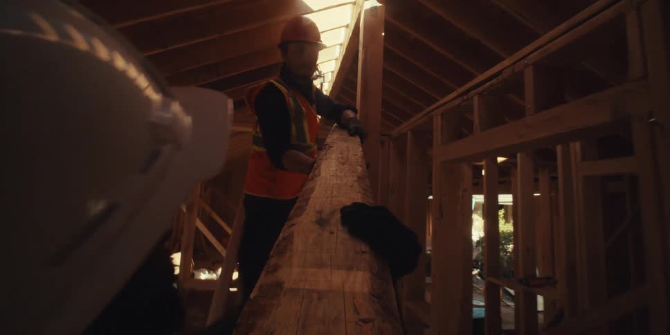 Two carpenters are carrying a four by four stud and lifting it towards the ceiling on a construction site