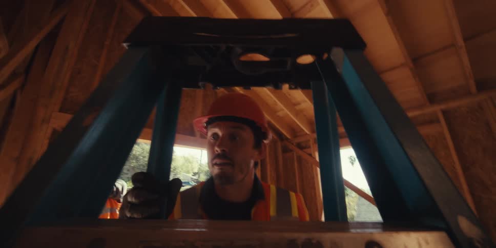 A construction worker brings a ladder inside and climbs on it while other workers take measurements
