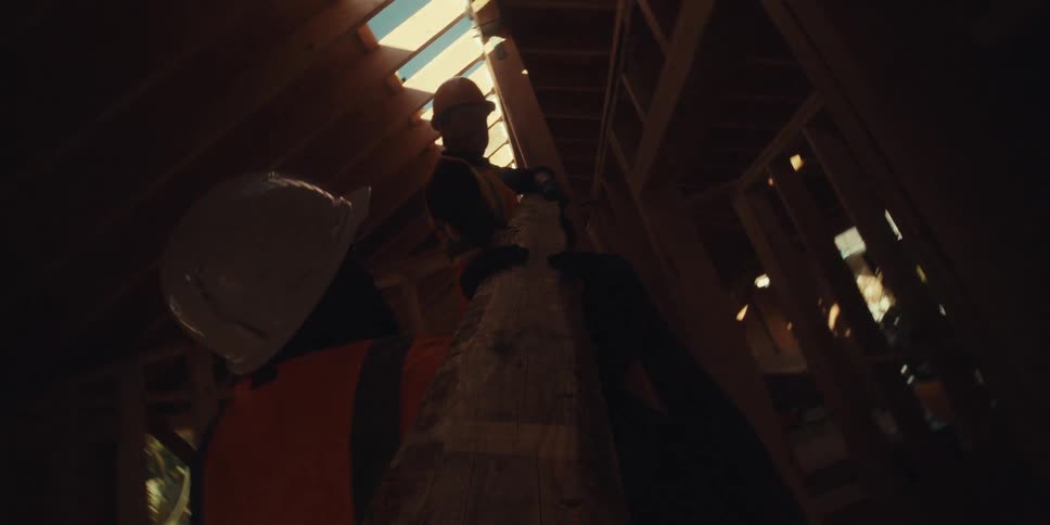 Two construction workers place a wooden beam onto the framework of a house under construction