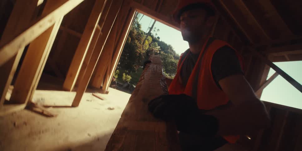 A construction worker wearing a hardhat lifts a large wooden beam