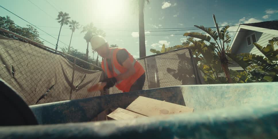 A construction worker tosses scrap wood into a wheelbarrow at a construction site